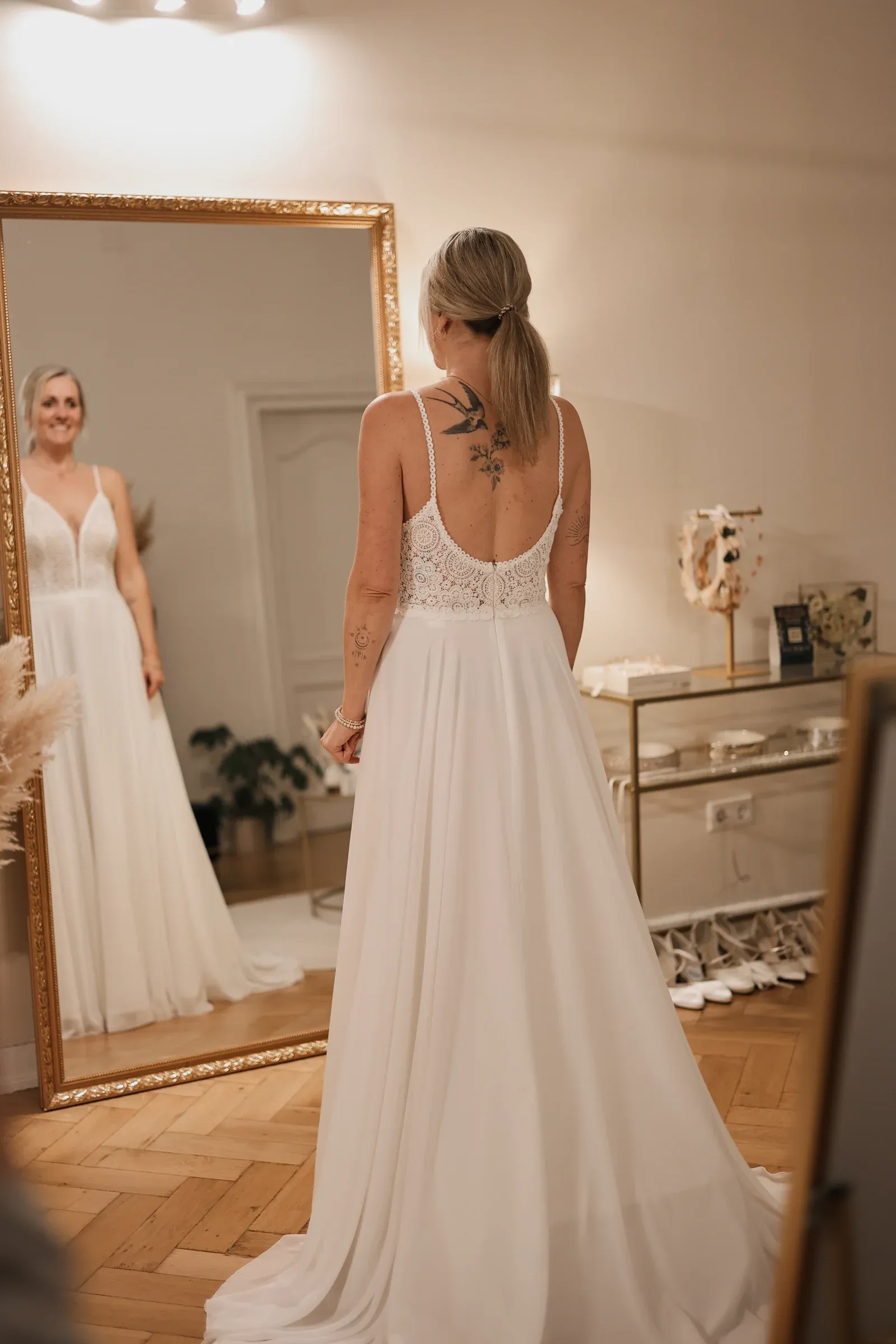 Eine Braut betrachtet ihr Spitzenkleid im großen Spiegel der Boutique