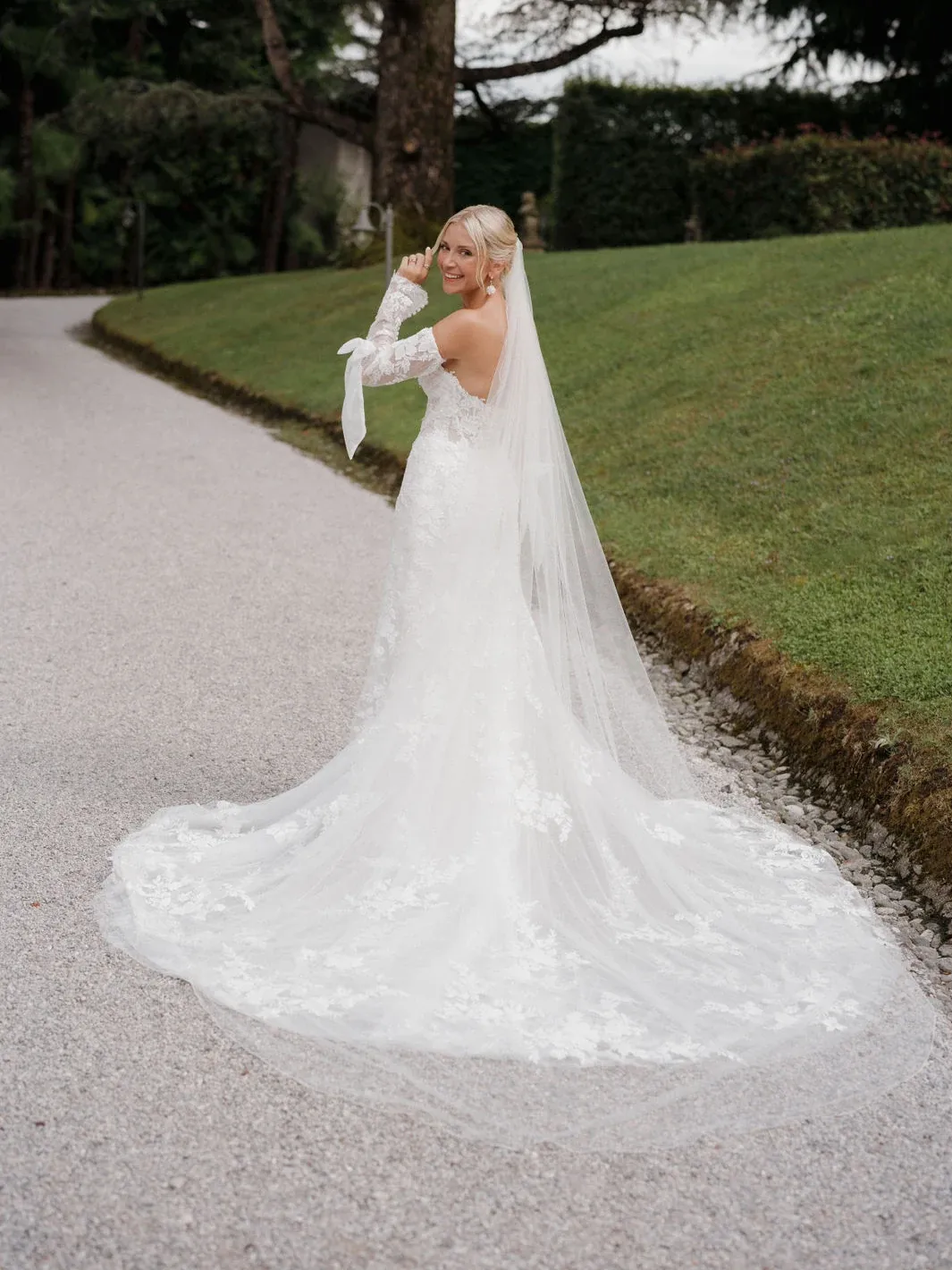 Braut mit langem Schleier über einem Spitzenkleid auf einem Gartenweg